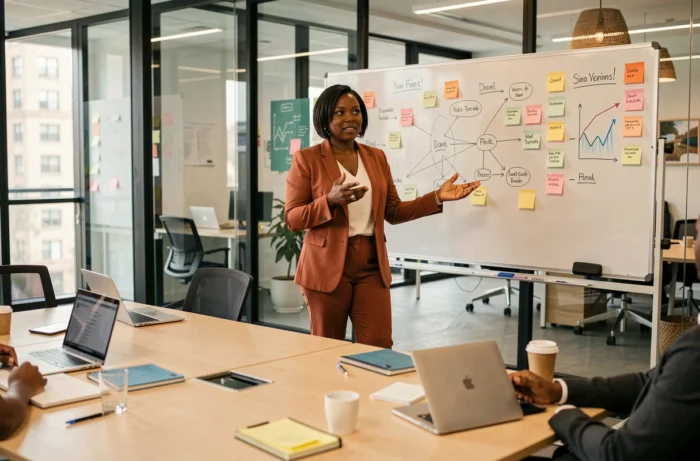 Femme cheffe d'entreprise afro-descendante présentant une stratégie business devant un tableau blanc dans une salle de réunion de startup
