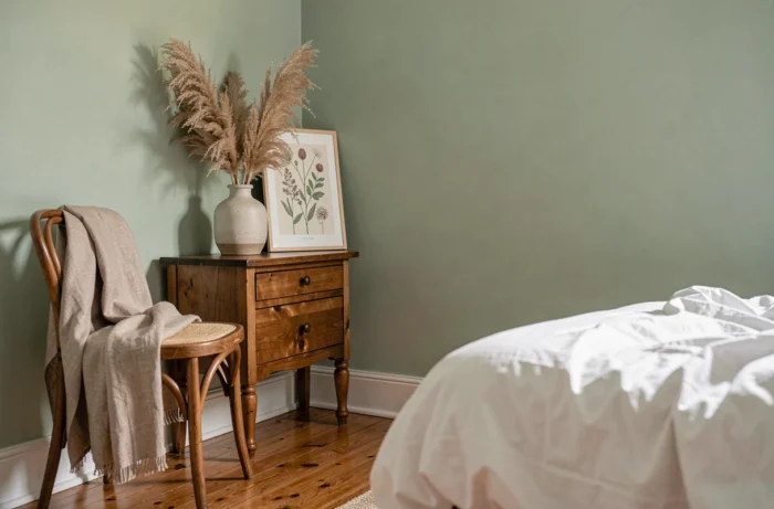Coin chambre décoré avec une table de nuit en bois vintage, un vase en céramique avec herbes de la pampa et un imprimé botanique encadré